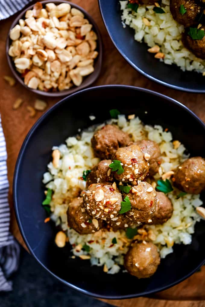 An overhead view of a bowl of Slow Cooker Thai Chili Peanut Meatballs with a small bowl of peanuts to garnish.