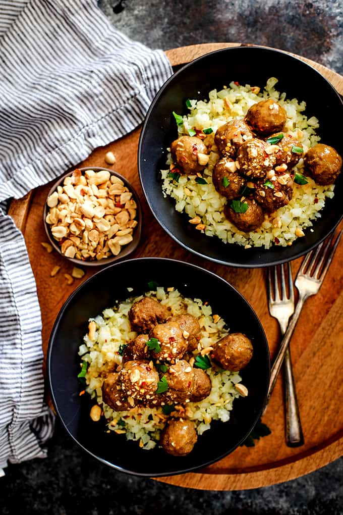Two bowls of Slow Cooker Thai Chili Peanut Meatballs sit on a wooden tray flanked by a striped napkin.