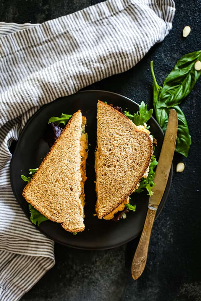 An overhead view of a sliced Apricot Basil Chicken Salad Sandwich on a plate with a knife.