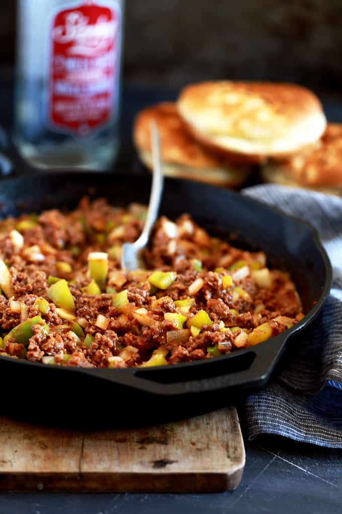 A skillet of Easy Sloppy Joes with a spoon sits on a wooden serving board.