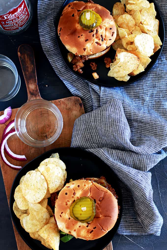 An overhead view of two plates of Easy Sloppy Joes sandwiches flanked by a striped napkin and two water glasses.