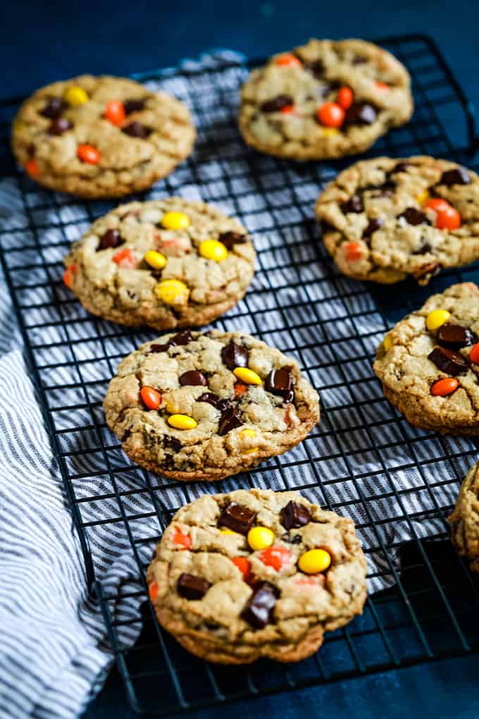 Reese's Pieces Chocolate Chip Cookies on a cooling rack over a white and grey striped napkin on a blue background.