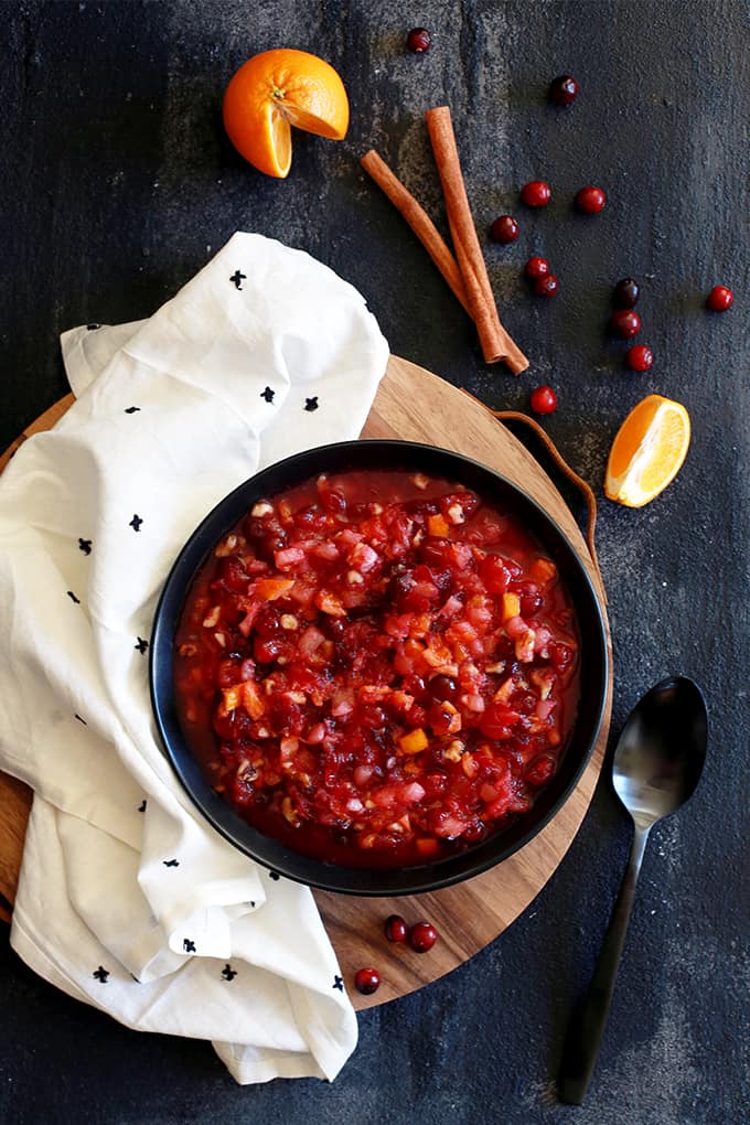 This amazing seven ingredient Citrus Cranberry Sauce is the easiest holiday side dish to grace your dinner table, with a bright and flavorful twist on an otherwise traditional dish. #cranberry #cranberrysauce #clementine #thanksgiving #thanksgivingrecipes #christmas #citrus An overhead shot of a bowl of Citrus Cranberry Sauce on a wooden platter flanked by a napkin, spoon, cinnamon sticks, cranberries and a clementine.