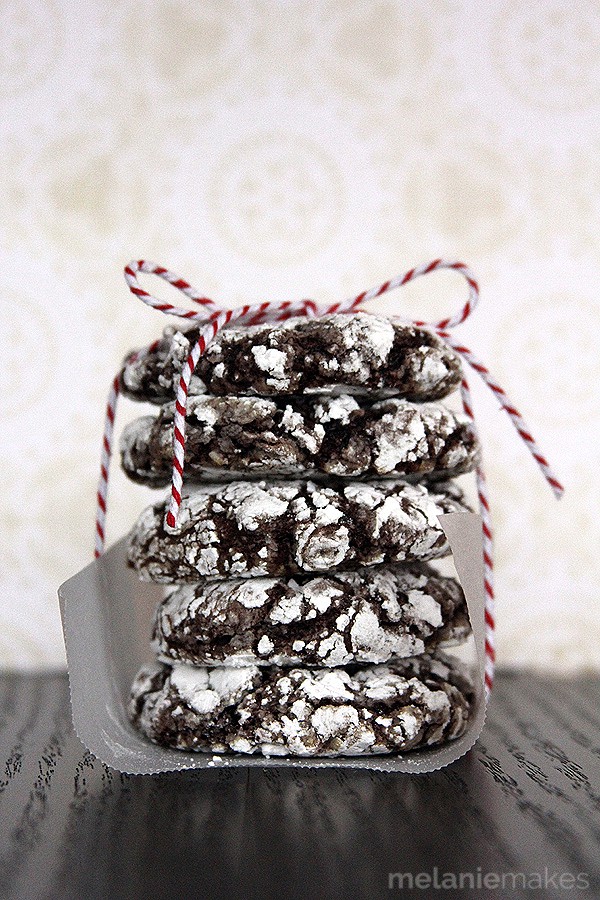 Five chocolate crinkle cookies are stacked on top of eachother. A red and white string is wrapped around to hold them in place.