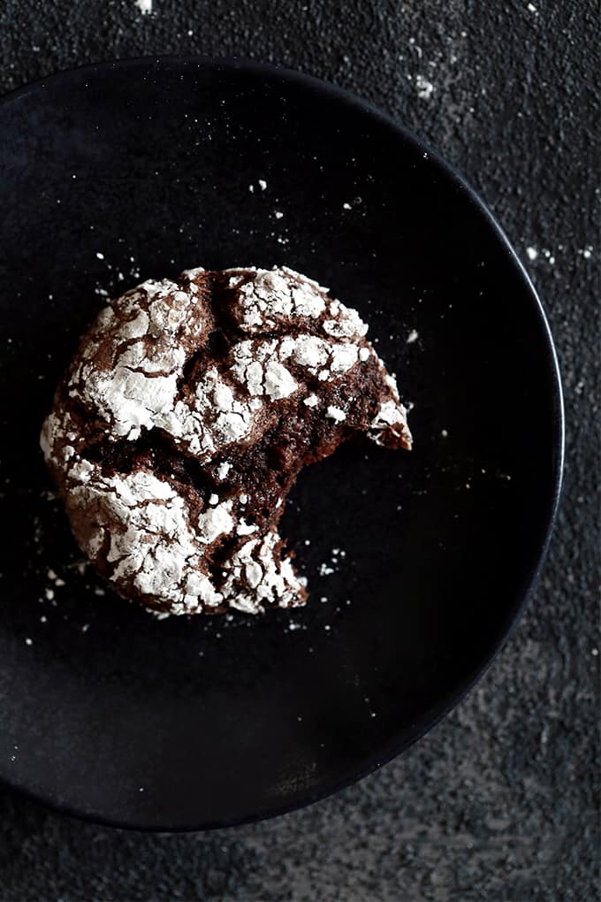 A Double Chocolate Ginger Crinkle Cookie sits on a black plate with a bite taken out of it.