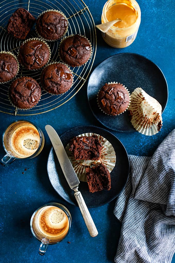 An overhead view of two black plates with Peanut Butter Mocha Chocolate Chip Muffins surrounded by coffee cups, a striped napkin and additional muffins.
