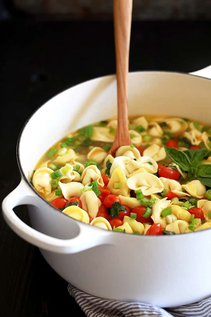 A wooden spoon rests in a pot of Cherry Tomato and Tortellini Soup.
