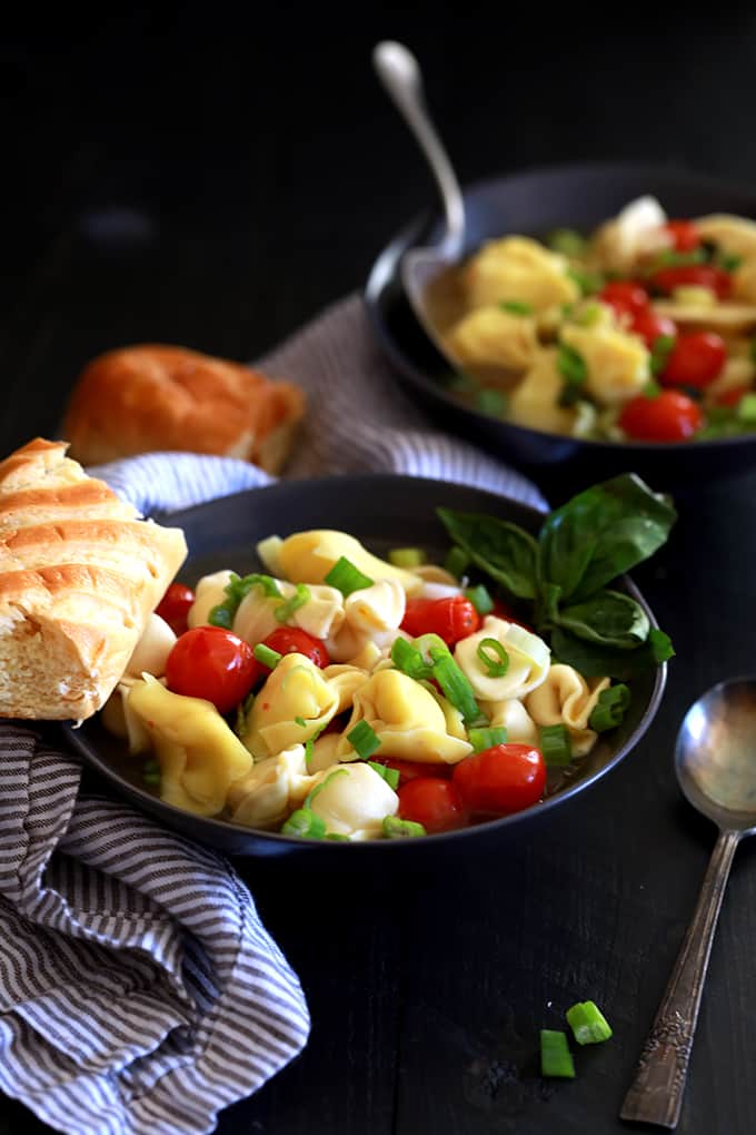 A piece of baguette rests on the side of a bowl of Cherry Tomato and Tortellini Soup.