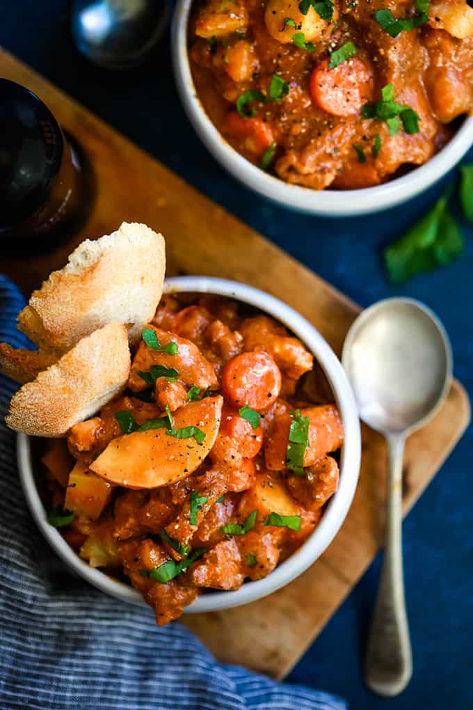 An overhead shot of two bowls of Stout Beer Beef Stew, one is sitting on a wood cutting board.