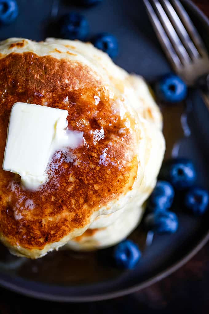 Butter melts on a stack of the Best Buttermilk Pancakes surrounded by blueberries.