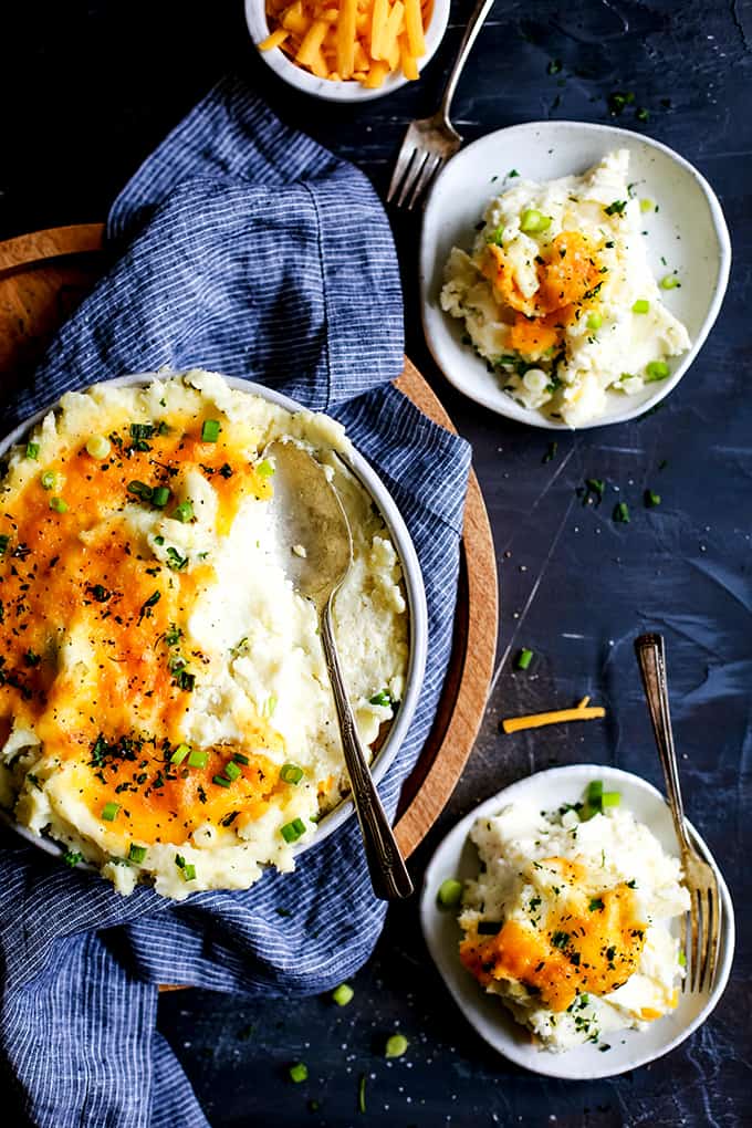 An overhead view of a bowl of Aunt Ruthie Mashed Potatoes with two plates full of potatoes.