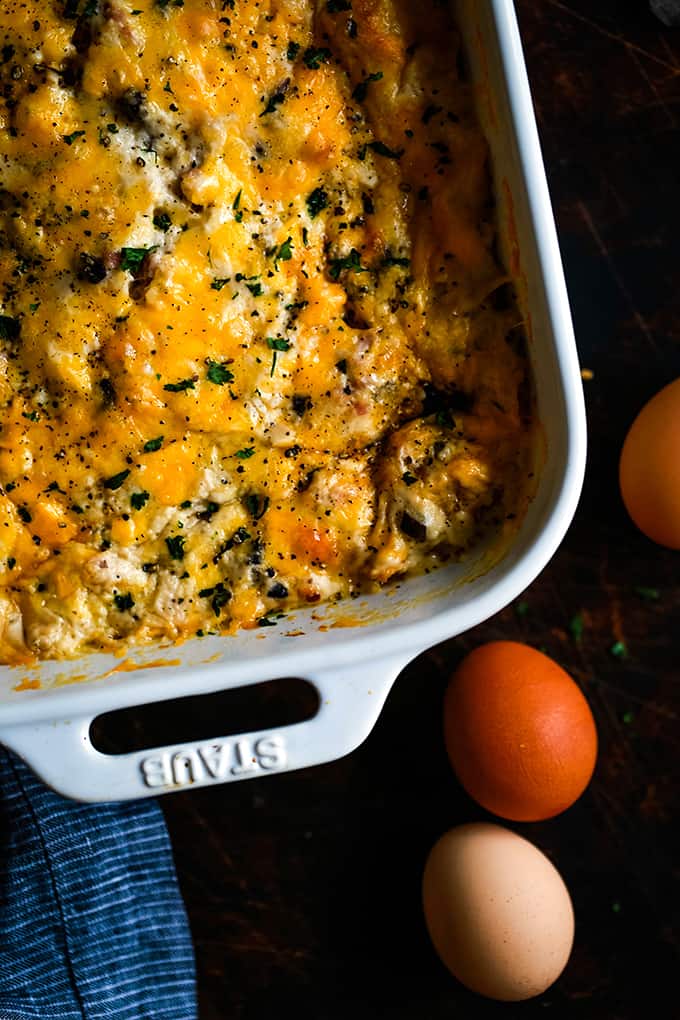 Bridge Brunch Casserole in a white baking dish surrounded by three eggs and a striped napkin.