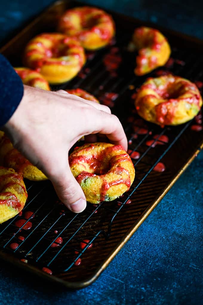 A hand grabs a Jelly Bean Donut off of a cooling rack.