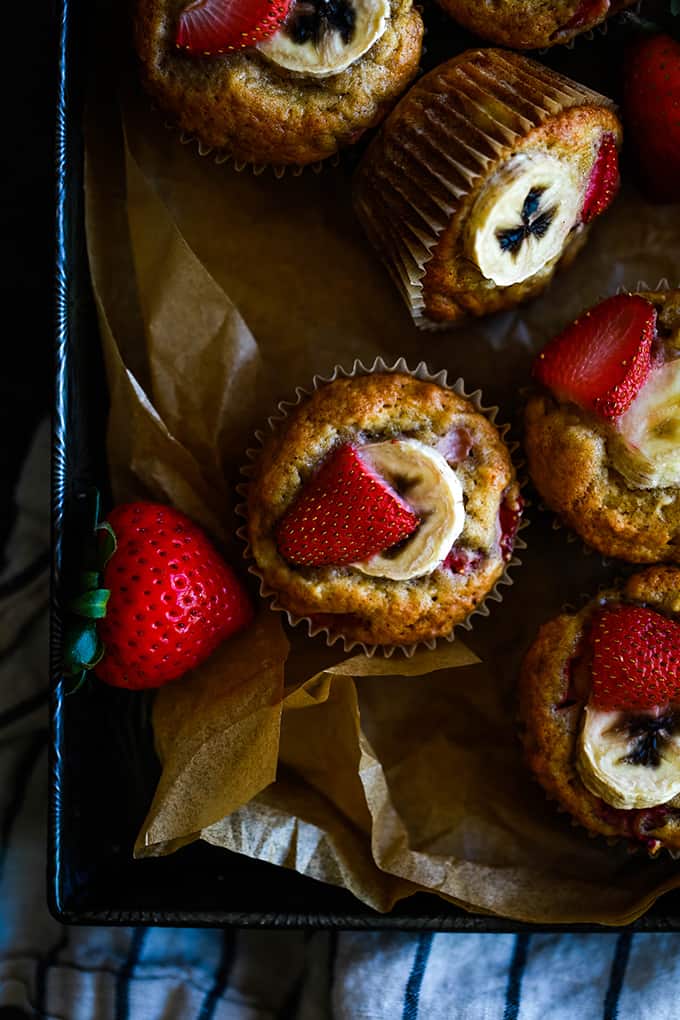 Strawberry Banana Muffins sit in a baking pan lined with parchment.