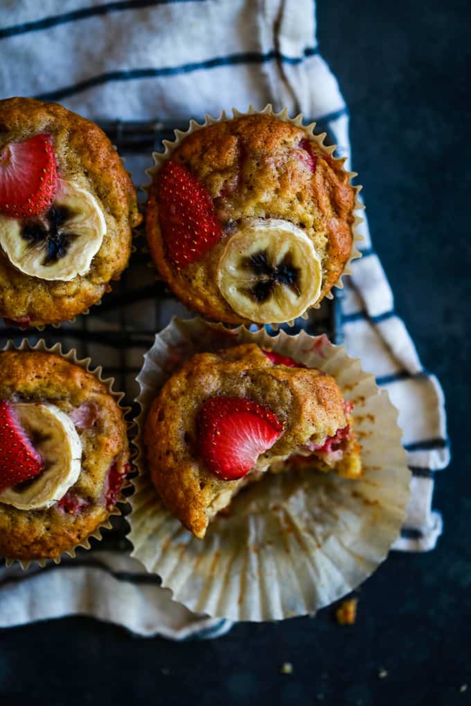 Four Strawberry Banana Muffins sitting on a striped napkin with a bite removed from one button.