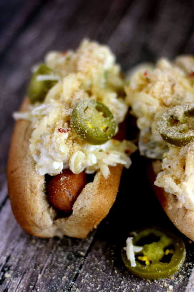 These Jalapeño Popper Mac and Cheese Brats are one of your favorite appetizers dressed up as a main dish. A grilled to perfection brat is nestled into a toasted bun and then topped with the cheesiest, meltiest, tastes just like a jalapeño popper mac and cheese. Each bratwurst is then garnished with additional shredded white cheddar jalapeño cheese, pickled jalapeños and toasted breadcrumbs. 