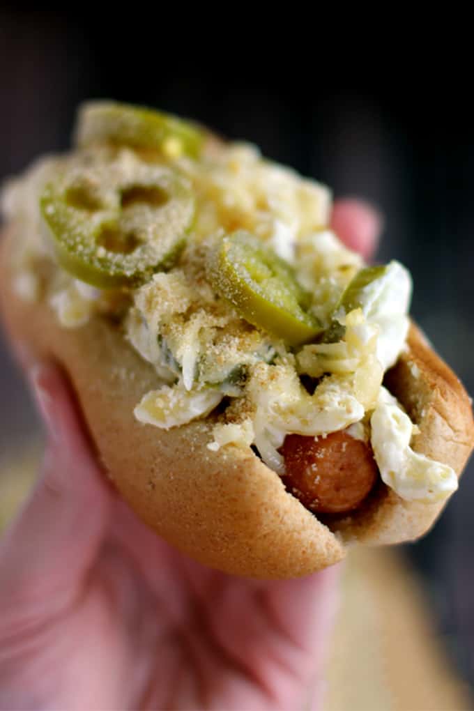 These Jalapeño Popper Mac and Cheese Brats are one of your favorite appetizers dressed up as a main dish. A grilled to perfection brat is nestled into a toasted bun and then topped with the cheesiest, meltiest, tastes just like a jalapeño popper mac and cheese. Each bratwurst is then garnished with additional shredded white cheddar jalapeño cheese, pickled jalapeños and toasted breadcrumbs. 