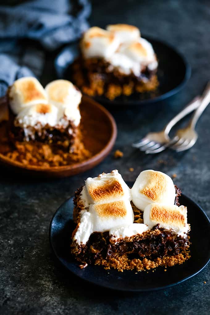 Three plates each with a Dulce de Leche Swirl S'mores Brownies sit on a black surface with two forks.