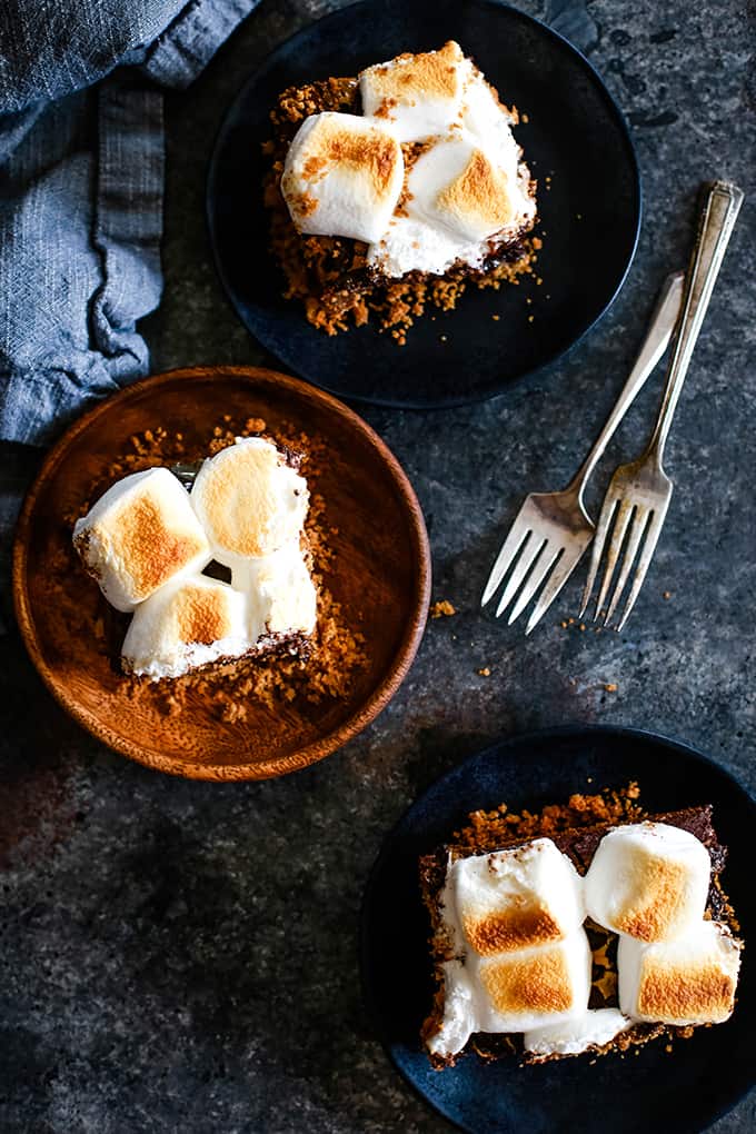 Three plates sit on a black background, each with a Dulce de Leche Swirl S'mores Brownie on it.