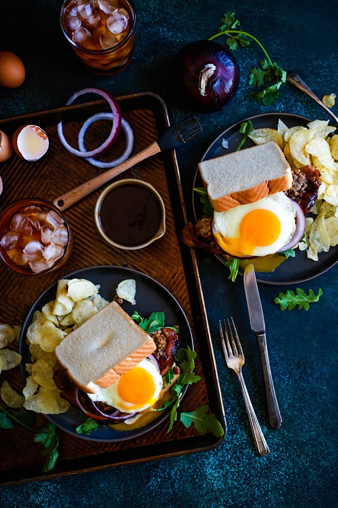 An overhead sho of two Grilled Barbecue Bacon Meatloaf SAndwiches plated with potato chips and all of the toppings.