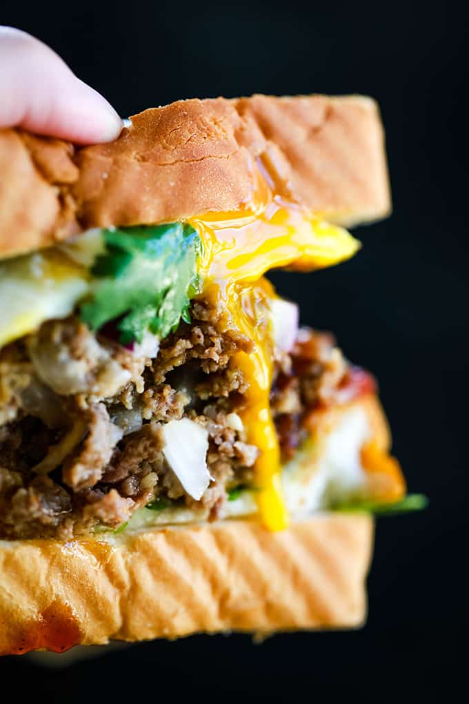 A hand holds a Grilled Barbecue Bacon Meatloaf Sandwich with an egg dripping down the side.