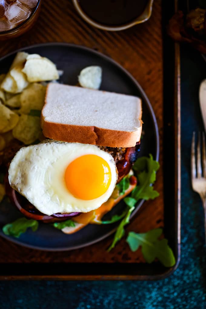 A sunny side up egg rests on the top of a Grilled Barbecue Bacon Meatloaf Sandwich.