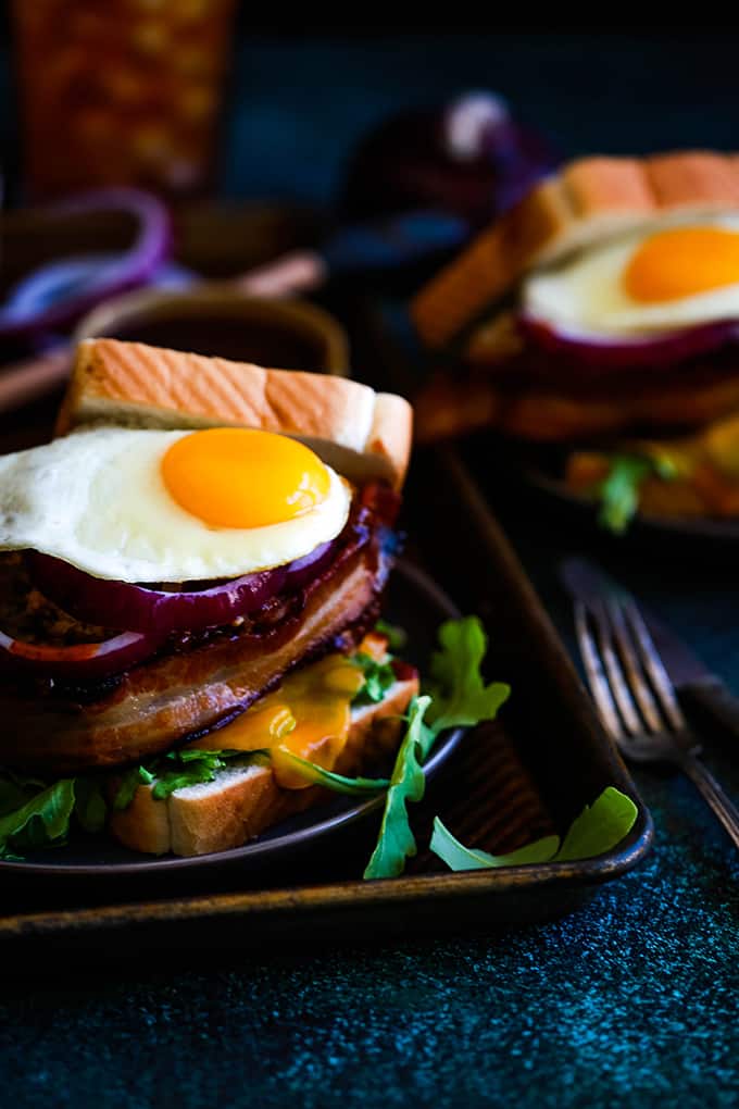 A Grilled Barbecue Bacon Meatloaf Sandwich is plated on a dark plate that sits on a sheet pan.