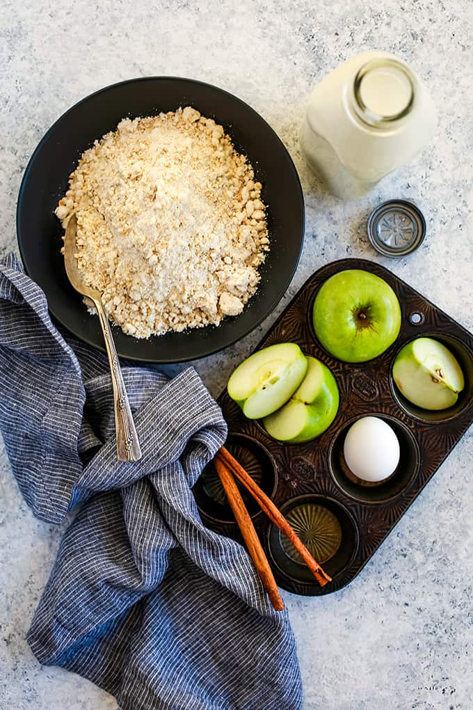 The ingredients required to make Cinnamon Apple Oatmeal Muffins on a white and grey background.