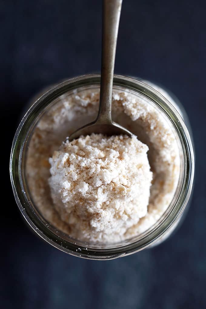 A spoon of Homemade Oatmeal Muffin Mix rests on the rim of a glass jar.