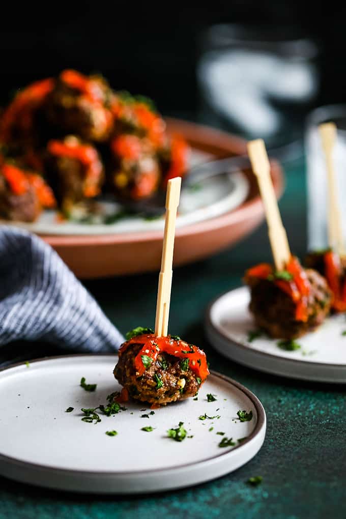 A Chili Garlic Meatball rests on a white plate with additional plates in the background.