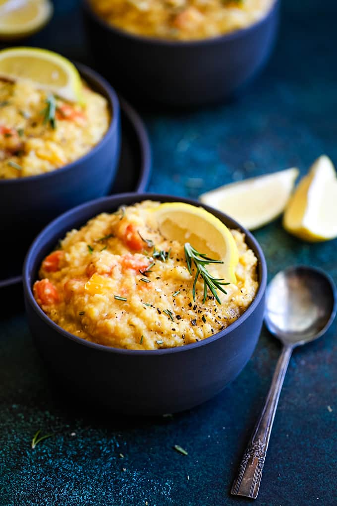 A bowl of Slow Cooker Lemon Rosemary Lentil Soup with a spoon and wedges of lemon.