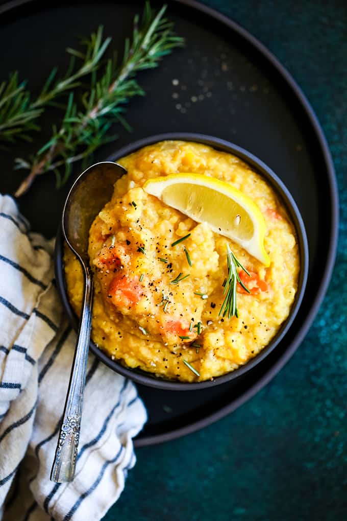 A bowl of Slow Cooker Lemon Rosemary Lentil Soup on a tray with a spoon, striped napkin and rosemary sprigs.