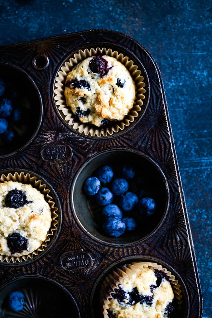 With a stir of a spoon and just four ingredients, you’ll be ready to put these Yogurt Blueberry Oatmeal Muffins in the oven before it’s even preheated! #blueberry #yogurt #oatmeal #muffins #breakfast #brunch An overhead view of three Yogurt Blueberry Oatmeal Muffins and blueberries in a muffin tin.