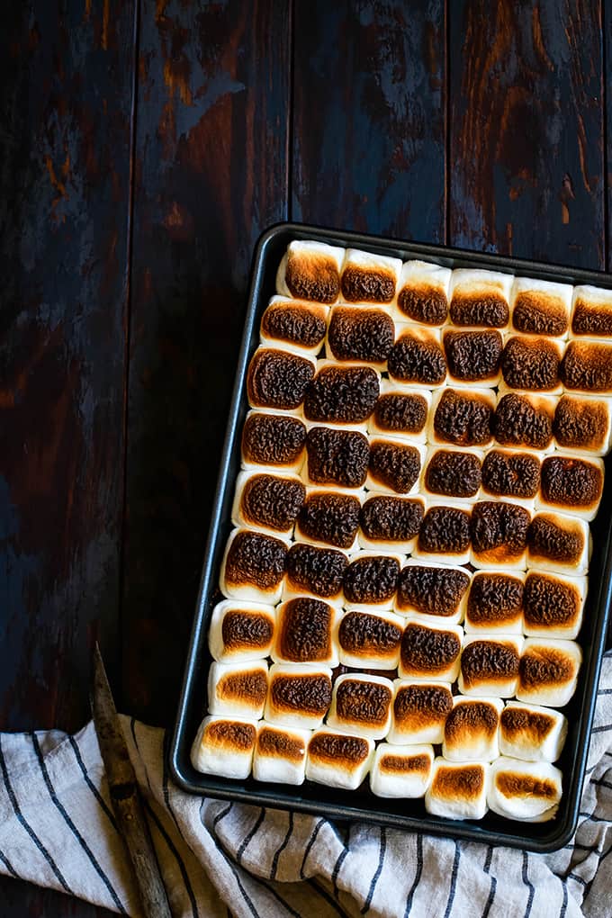 A pan of Peanut Butter Cup Stuffed S'mores Brownies on a wood surface with a striped napkin.