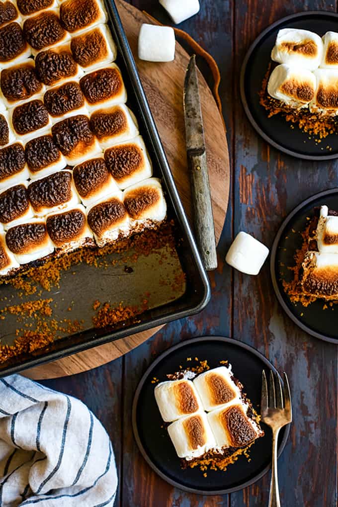 An overhead shot of a pan of Peanut Butter Cup Stuffed S'mores Brownies and three plates each with a brownie on them.