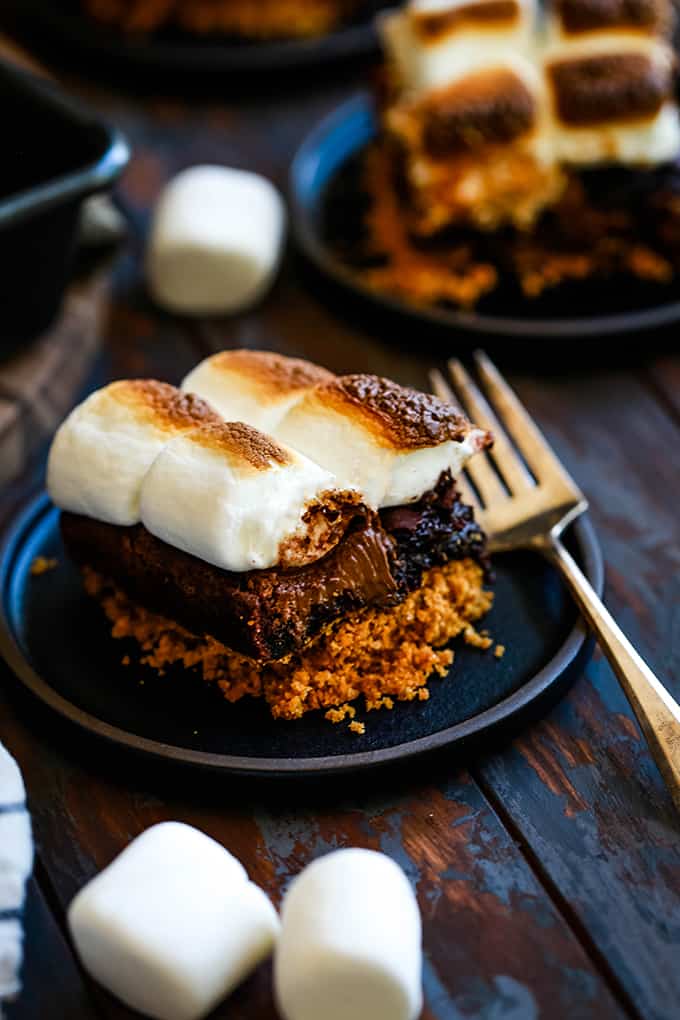 A Peanut Butter Cup Stuffed S'mores Brownie on a black plate with a fork.