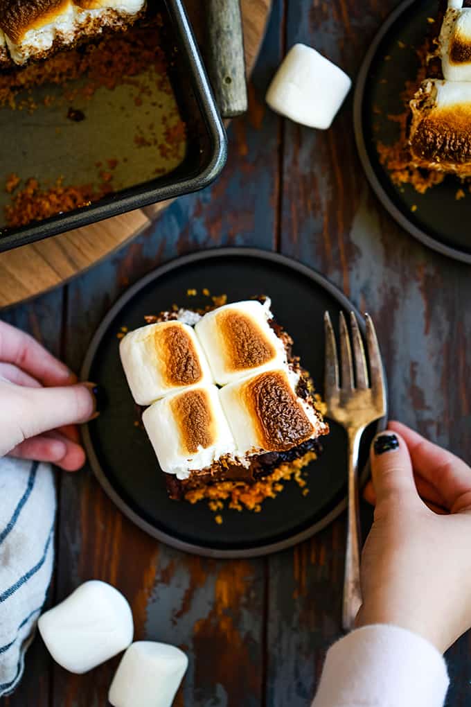 Two hands hold a black plate with a Peanut Butter Cup Stuffed S'mores Brownie.