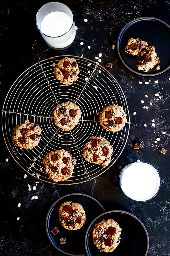 Oatmeal Raisin Chocolate Chip Cookies on a circular cooling rack and black plates with two glasses of milk.