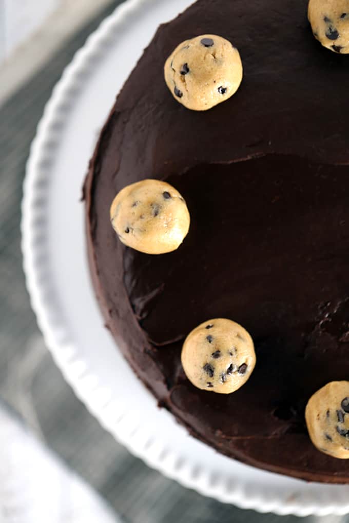 This Double Chocolate Peanut Butter Chocolate Chip Cookie Dough Cake is what peanut butter and chocolate lovers dream about. Creamy and studded with mini chocolate chips, a thick layer of peanut butter cookie dough is sandwiched between two layers of chocolate cake. The entire cake is then cloaked in a rich, whipped chocolate ganache frosting before being crowned with additional spheres of cookie dough. 