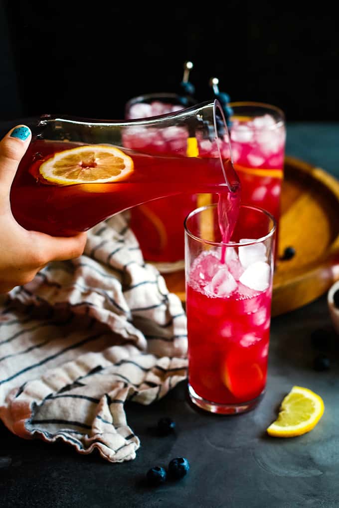 Blueberry Lemonade is poured from a pitcher into a glass of ice.