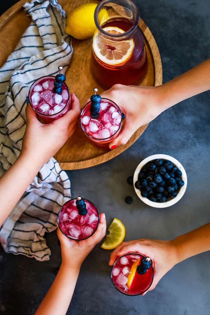 Four hands reach for glasses of Blueberry Lemonade.