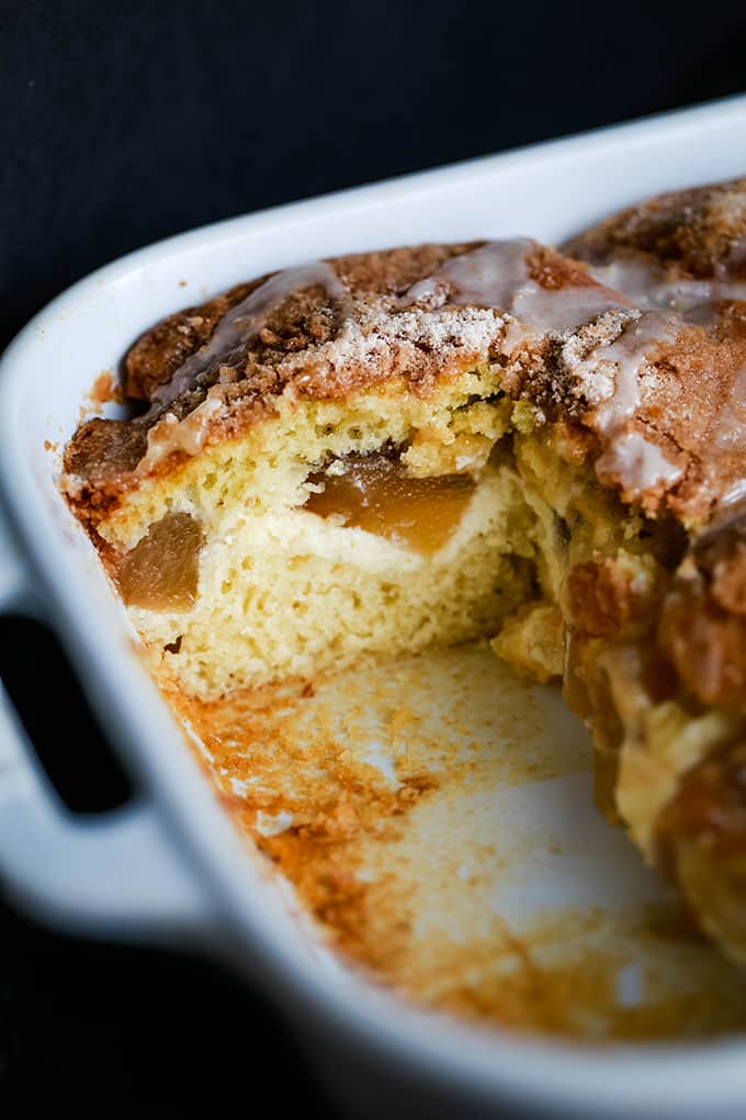 A baking pan of Caramel Apple Cheesecake Coffee Cake with pieces removed so that you can see the cheesecake swirl and apples that are in the middle of the coffee cake.