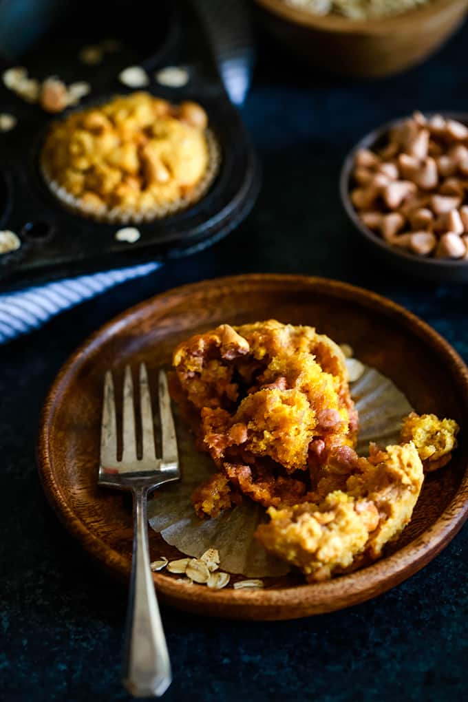 A Pumpkin Butterscotch Oatmeal Muffin is pulled apart and sits on a wooden plate with a fork.
