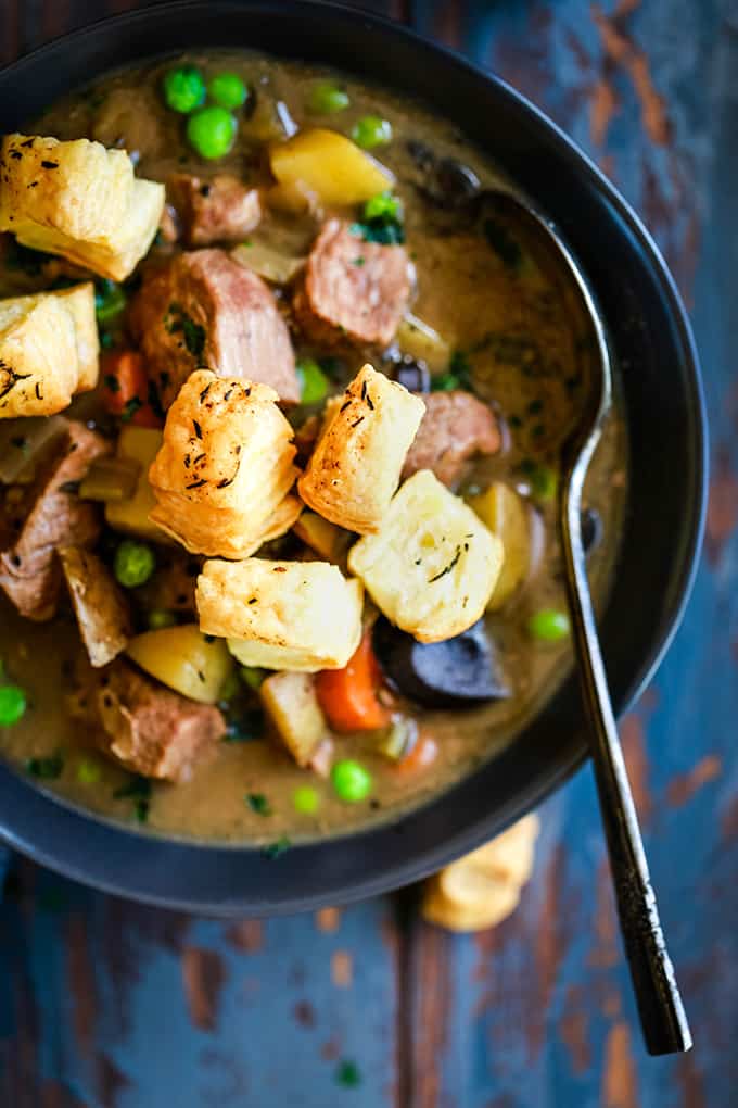 An overhead view of a bowl of Slow Cooker Beef and Guinness Pot Pie Soup with Thyme Puff Pastry Croutons with a spoon.