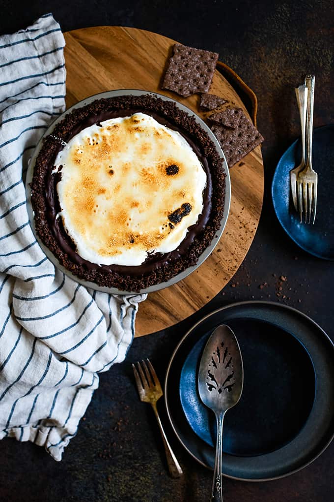 An overhead view of a Double Chocolate No Bake S'mores Pie on a wooden tray surrounded by plates.