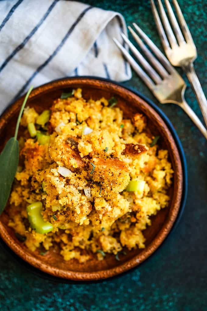 A wooden plate full of Slow Cooker Cornbread and Sausage Stuffing flanked by two forks and a striped napkin.