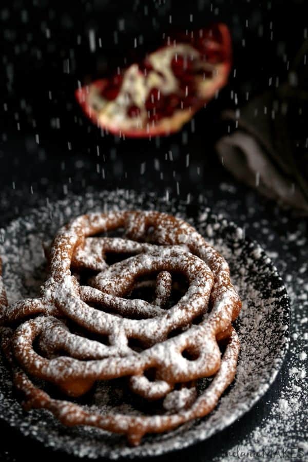 These Mini Eggnog Funnel Cakes are sure to be the star of any holiday party or gathering. A cinnamon eggnog batter is fried into a web of interlacing circles before being topped by a snow shower of powdered sugar and studded with pomegranate arils (seeds) for the perfect pop of holiday color. 