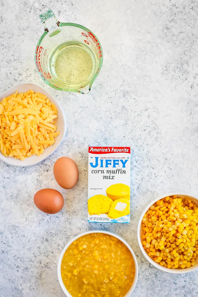 All of the ingredients needed to create Cheesy Corn Casserole sitting on a white speckled background.