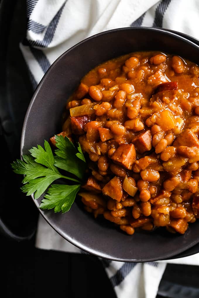 A bowl of Slow Cooker Smoky Baked Beans garnished with a sprig of parsley.