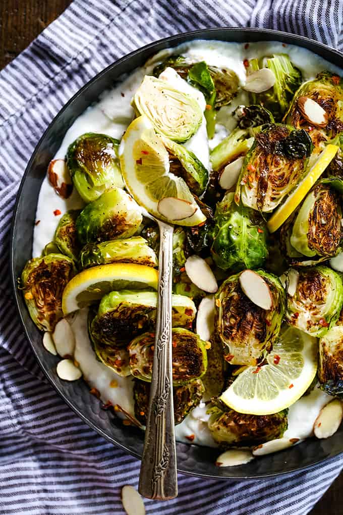 A serving spoon rests in a bowl of Roasted Brussels Sprouts with Lemon and Greek Yogurt.